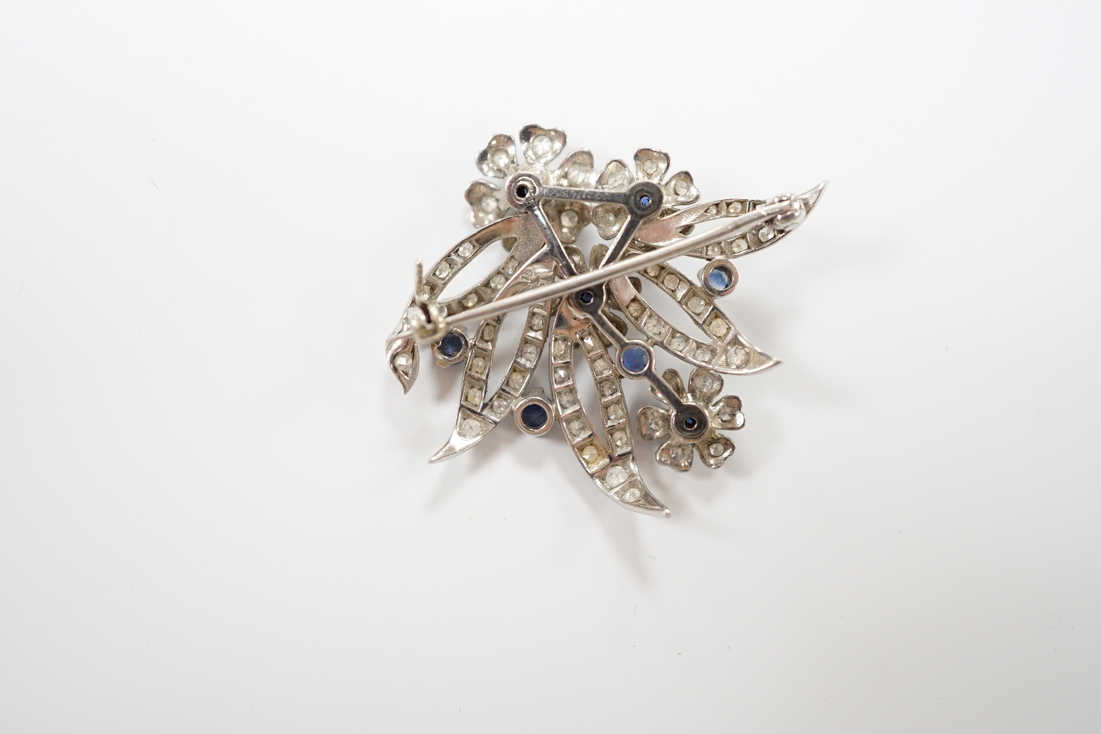 A white metal (stamped 18 plat), sapphire and diamond chip cluster set foliate brooch, 32mm, gross weight 11 grams.